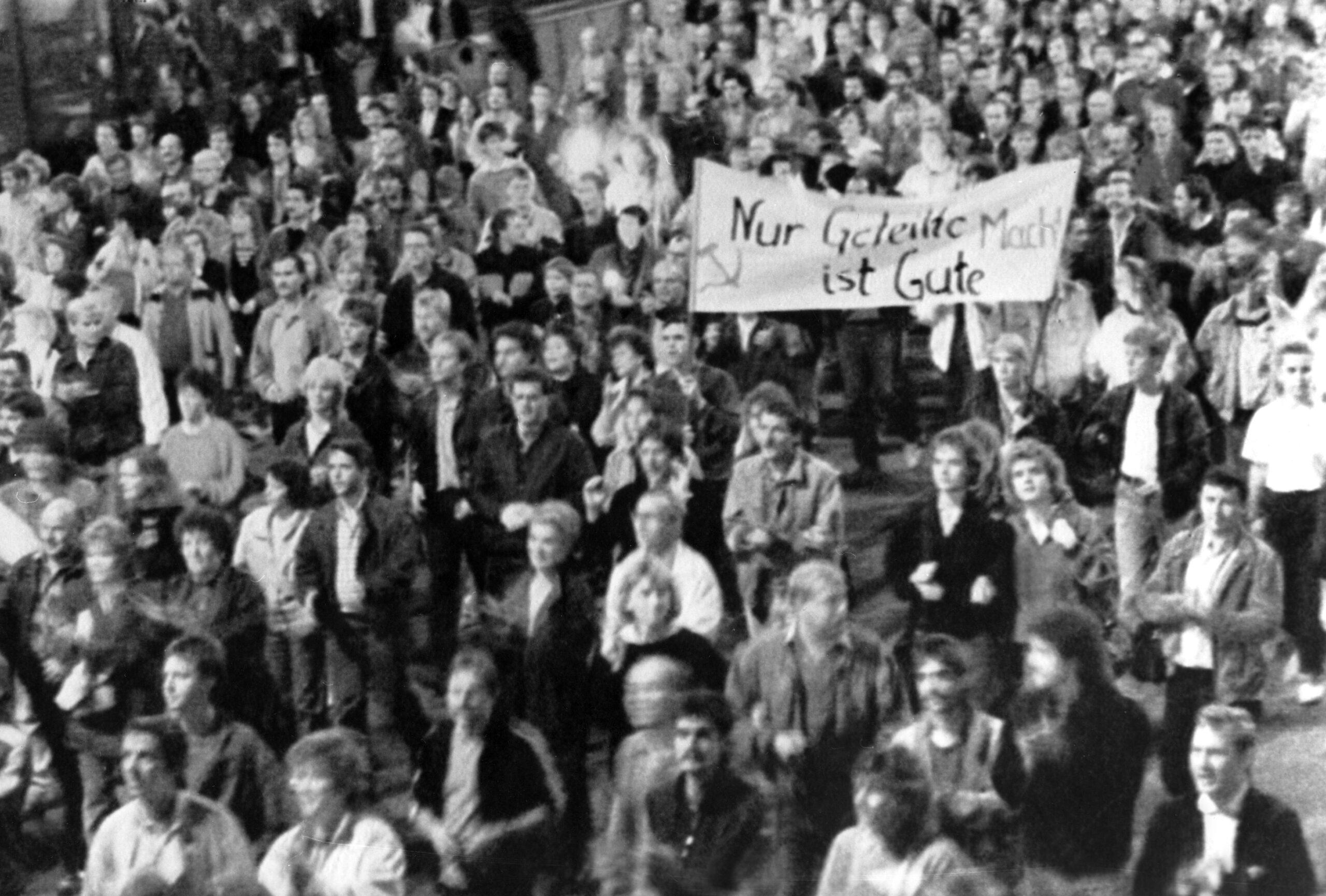 Schwarz-Weiß Fotografie einer Demonstration 1989. Auf einem Schild steht: "Nur Geteilte Macht ist Gute."
