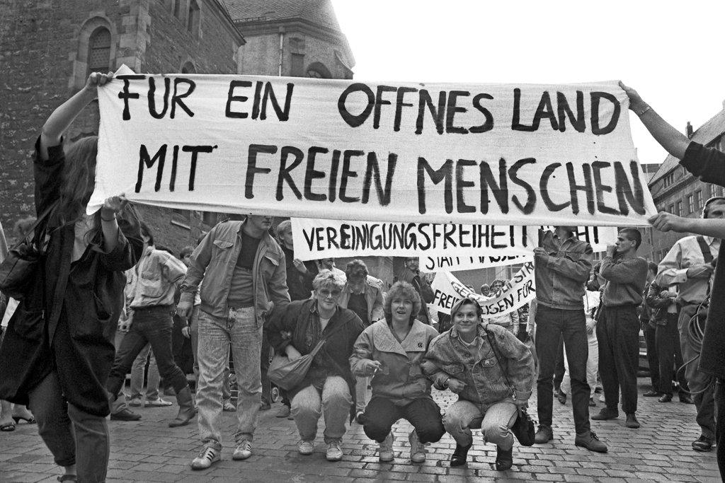 Schwarz-weiß-Fotografie einer Demonstration vom 4. September 1989: Menschen halten ein großes Transparent mit der Aufschrift "Für ein offenes Land mit freien Menschen", darunter kleinere Schilder mit "Vereinigungsfreiheit".